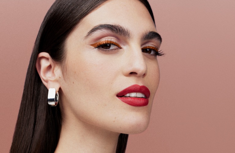 Mulher de perfil posando para a foto, usando um batom matte vermelho e maquiagem em tons terrosos