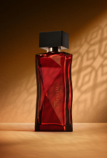 Deo Parfum Essencial Safran Feminino em frasco facetado vermelho com tampa preta. Está em fundo cor areia com sombra geométrica projetada.