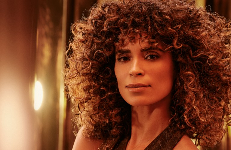 mulher com cabelo cacheado de perfil com a mão no ombro