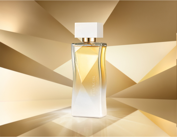 Frasco de Essencial Exclusivo Floral Feminino, em tons de branco e dourado, aparece em destaque no centro da tela sobre fundo multifacetado dourado, fazendo alusão ao design do frasco de Essencial.