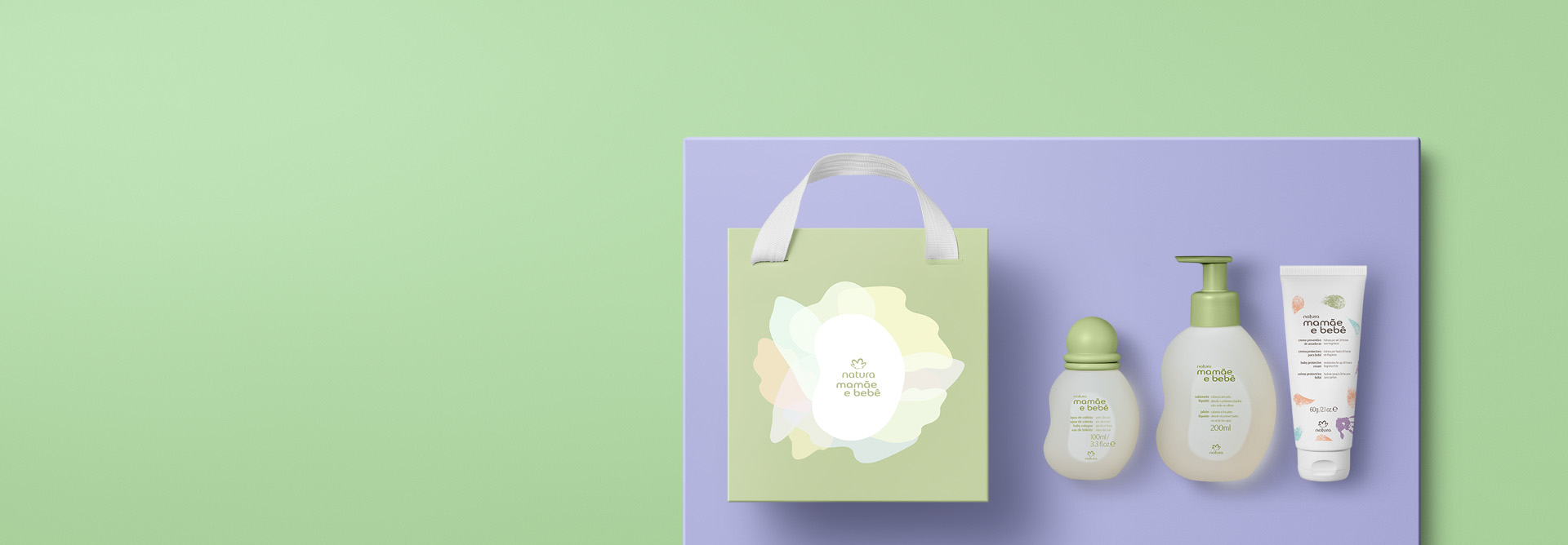 Presente Natura Mamãe e Bebê Momento Chá de Bebê, incluindo 1 água de colônia, 1 sabonete líquido, 1 creme preventivo de assaduras e 1 sacola em destaque sobre retângulo azul-claro. Fundo verde-claro.