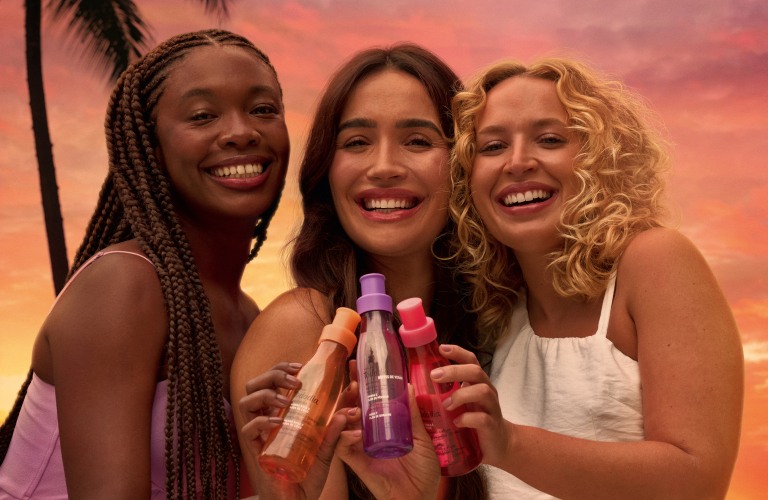 3 mulheres brindando com seus body splashes para os cuidados com a pele no verão