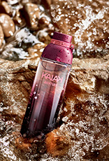 Frasco de Kaiak Aventura feminino em verde sobre pedras molhadas com água corrente e respingos.