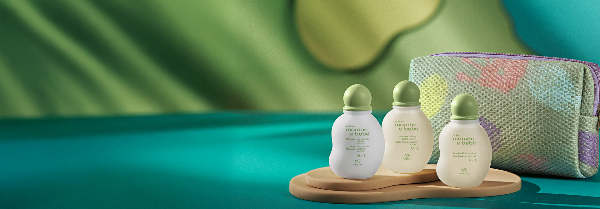 Kit Miniatura Natura Mamãe e Bebê, com Água de Colônia sem Álcool, Sabonete Líquido, Hidratante e Nécessaire colorida, destaca-se sobre bandeja de madeira em superfície azul e fundo verde vibrante.