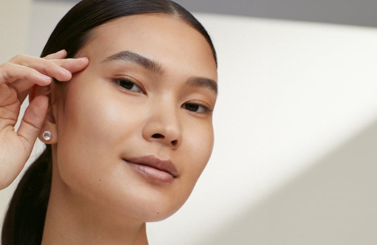 Mulher asiática com a mão direita na lateral do rosto. Ela está usando um rabo de cabalo