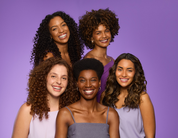 Foto de 5 mulheres com cabelos de diferentes curvaturas de cacheados e crespos,  em fundo roxo.
