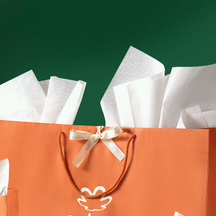 Sacola de presente da Natura com laço e papel de seda saindo da sacola. A sacola está sobre fundo verde.