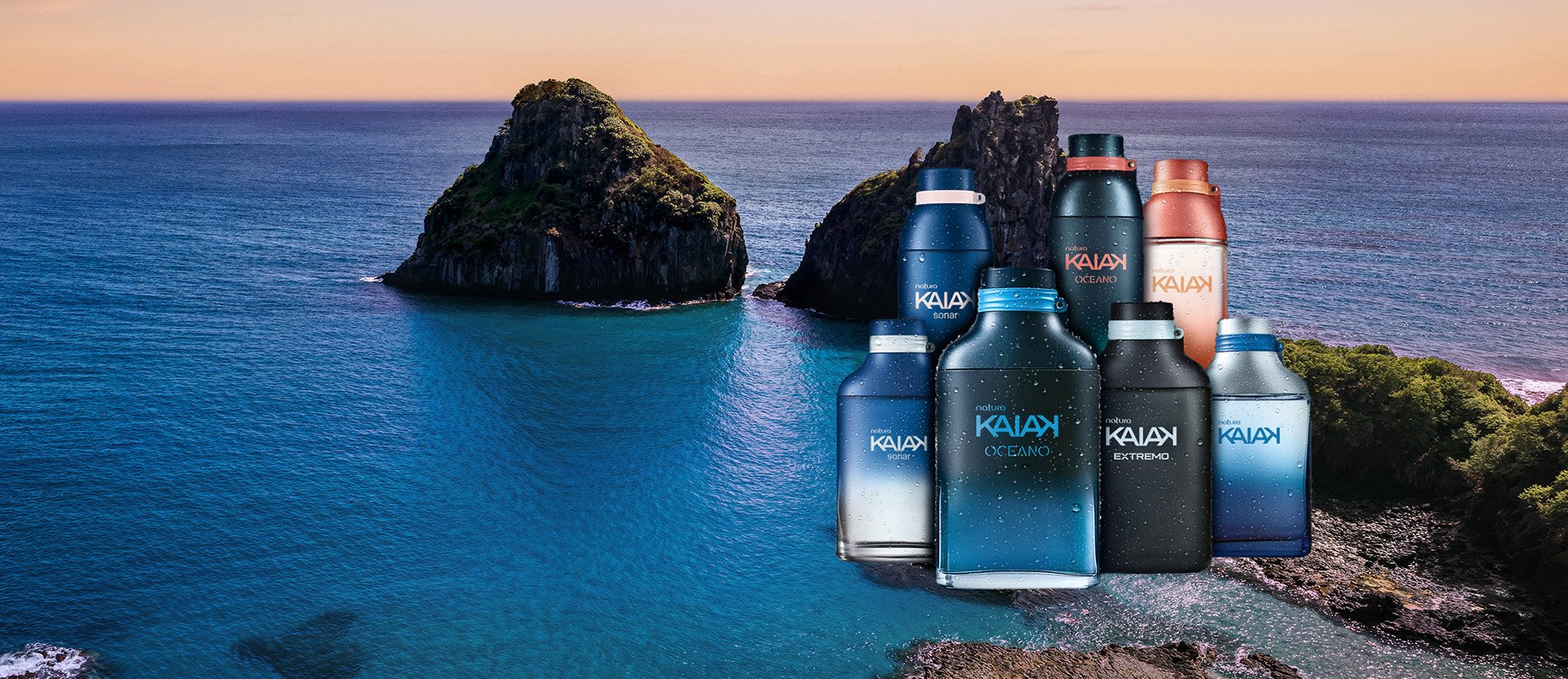 Frascos de fragrâncias Kaiak sobre a água azul do mar, com ilhas rochosas e céu em tons de azul e laranja ao fundo. 