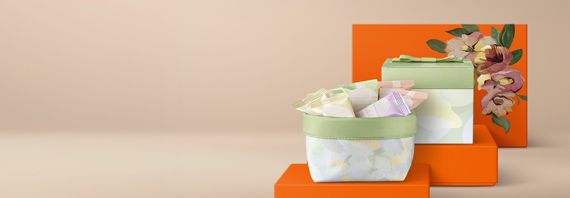 Cesta de tecido verde-claro com minissabonetes em tons pastel destaca-se ao lado de uma caixa com tampa verde-claro e laço sobre caixas de presentes laranjas com ilustração floral.