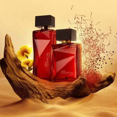 Deos Parfum Essencial Safran Feminino e Essencial Safran Masculino, ambos em frascos vermelhos com tampas pretas. Estão em um tronco na areia, com flores amarelas e fios de açafrão vermelho ao redor.