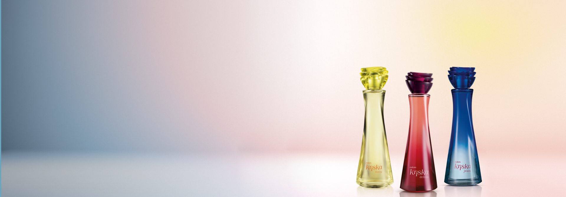 Desodorantes Colônia da linha Kriska, Flores, Delírio e Jeans, em fundo em degradê levemente multicolorido. Embalagens de vidro, com tampa em formato de flor nas cores amarelo, vermelho e azul.