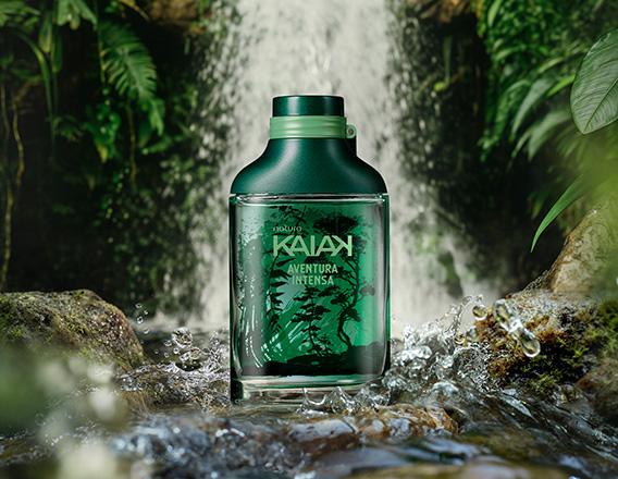 Frasco de Kaiak Aventura Intensa masculino em verde sobre pedras na frente de uma cachoeira cercada por folhagens.