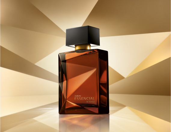 Frasco de Essencial Intenso Masculino, em tons de âmbar e marrom e tampa preta, aparece em destaque em fundo dourado multifacetado, fazendo alusão ao design dos frascos de Essencial.