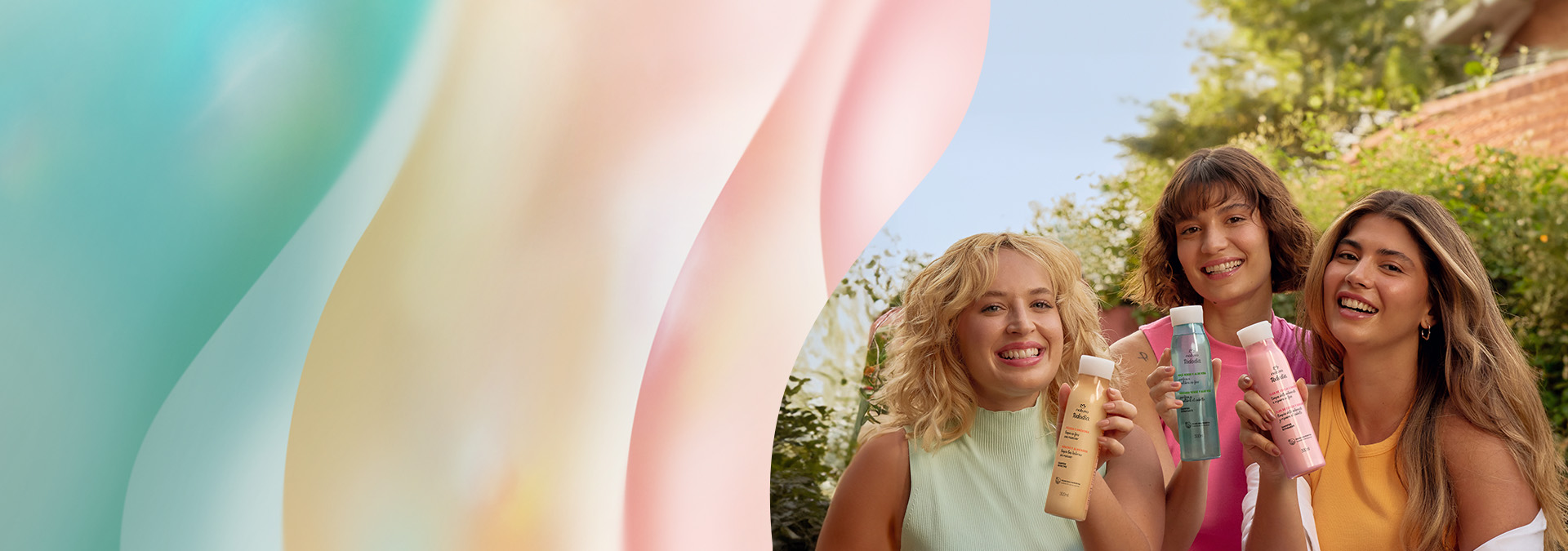 3 mulheres jovens e sorridentes seguram produtos de Tododia Cabelos. Elas estão sentadas em um jardim com árvores ao fundo.