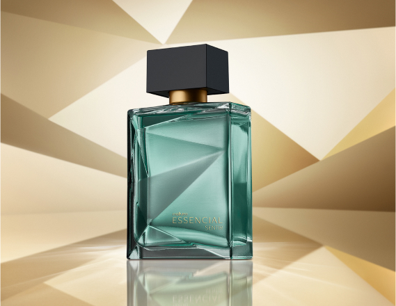 Frasco de Essencial Sentir Masculino, em tom de verde-água e tampa preta, aparece em destaque em fundo dourado multifacetado, fazendo alusão ao design dos frascos de Essencial.