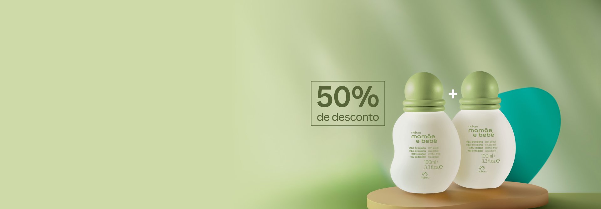 Águas de Colônia Natura Mamãe e Bebê lado a lado com sinal "+" sobre forma em madeira. Fundo em tons de verde. Selo retangular “50% de desconto” à esquerda.