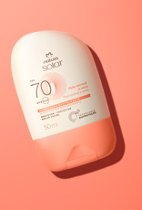 Embalagem creme com tampa laranja Natura Solar Facial FPS 70 para pele normal a seca, sobre fundo laranja.