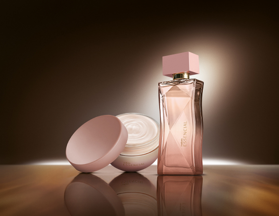 Na cena, Desodorante Hidratante Corporal Perfumado Essencial Feminino e Deo Parfum Essencial Feminino aparecem iluminados sobre superfície marrom em fundo escuro.