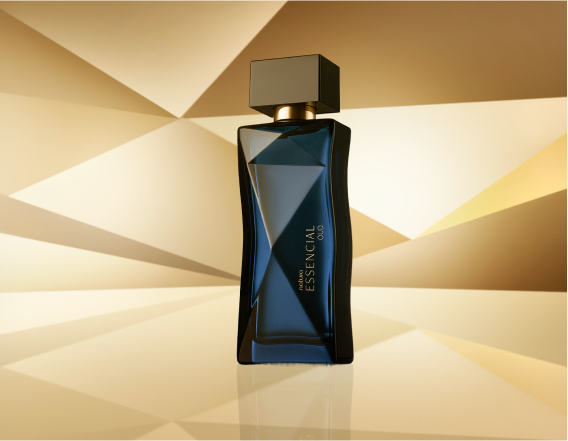 Frasco de Essencial Oud Feminino, em tom de azul-escuro e tampa preta, aparece em destaque no centro da tela sobre fundo multifacetado dourado, fazendo alusão ao design do frasco de Essencial.