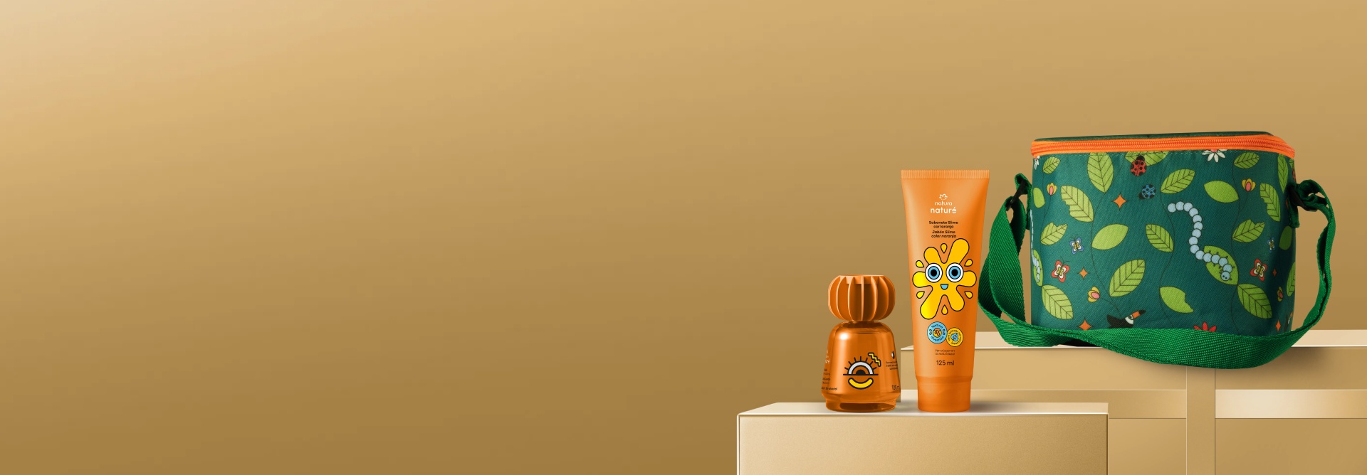Sabonete Slime e Colônia Pula Corda da linha Naturé ao lado de bolsa verde com estampa de folhas e insetos. Frascos laranja sobre caixas de presente e fundo dourados.
