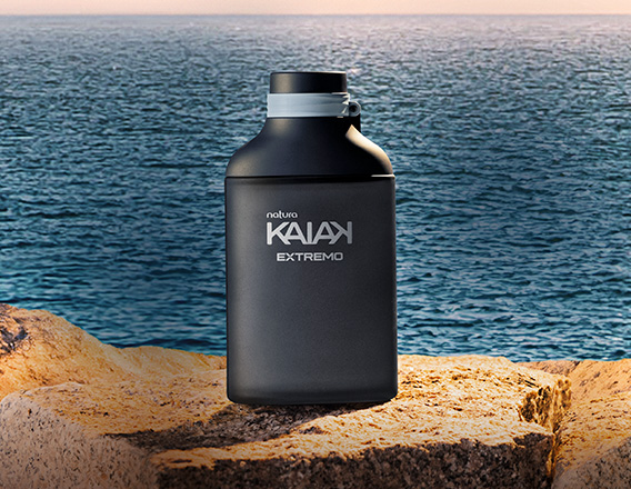 Frasco preto fosco da fragrância masculina Kaiak Extremo sobre rocha à beira do mar, com água azul e céu alaranjado ao fundo.