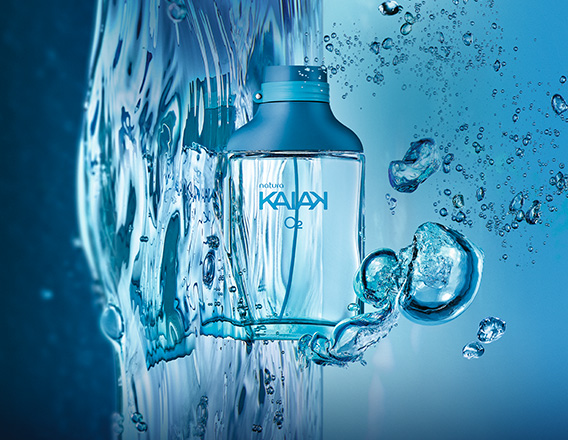 Frasco de Kaiak O2 masculino, em vidro translúcido, apoiado sobre água e respingos em fundo azul.