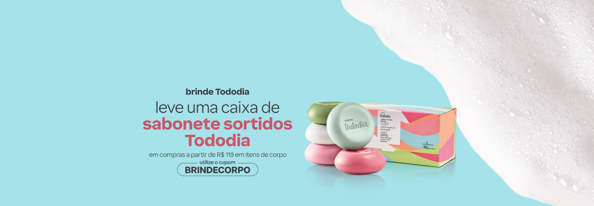 Sabonete em Barra Tododia, com 5 barras redondas coloridas, ao lado de uma caixa colorida sobre fundo azul-claro com espuma branca. Texto aplicado: brinde Tododia. Leve uma caixa de sabonete sortidos Tododia em compras a partir de R$ 119 em itens de corpo. Utilize o cupom BRINDECORPO.