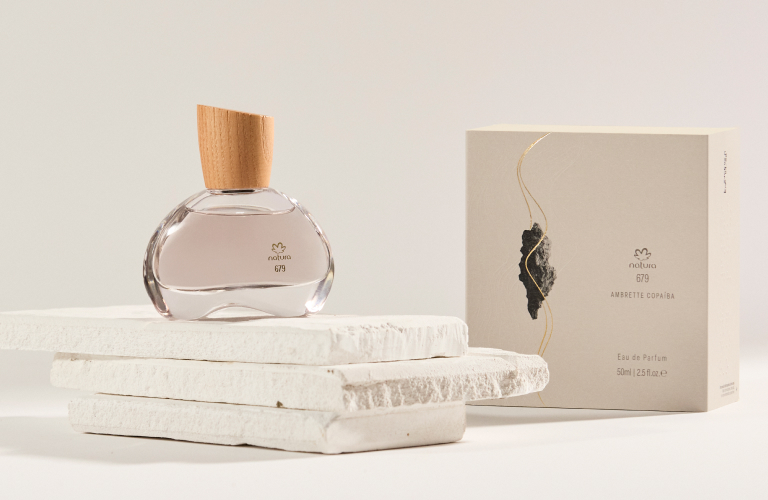 Frasco do Eau de Parfum Natura 679 Ambrette Copaíba ao lado de sua embalagem.