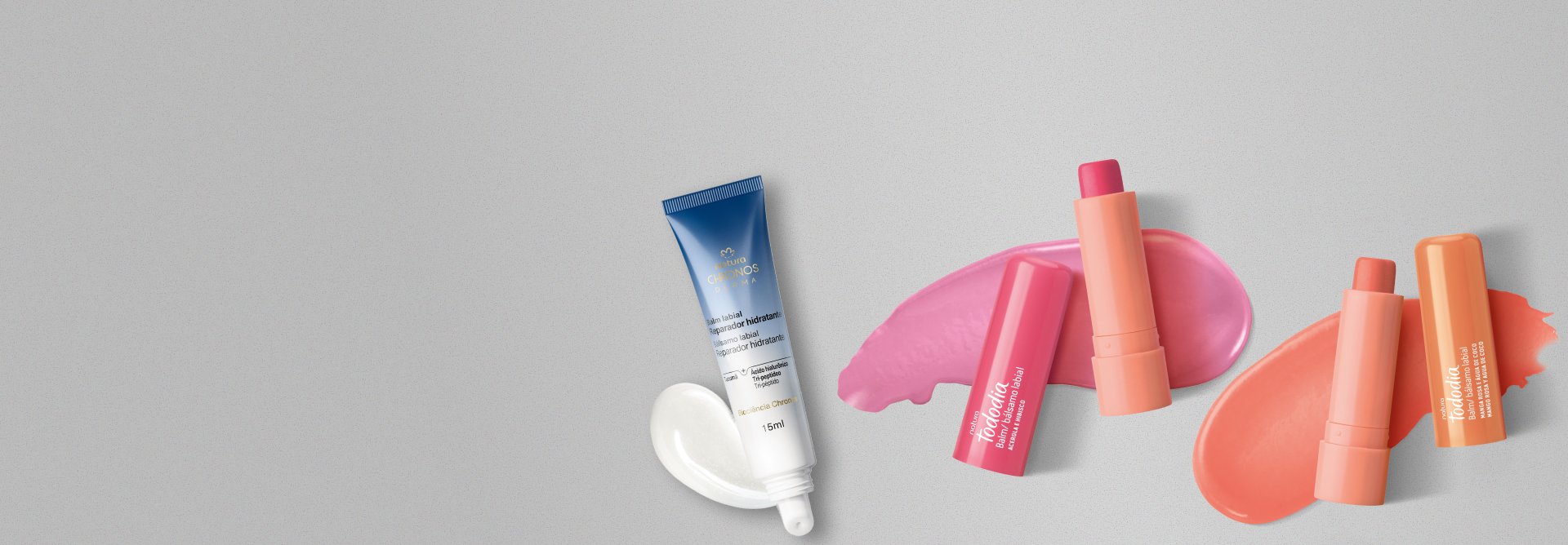3 balms labiais abertos sobre fundo cinza com produtos espalhados sob as embalagens. 1 balm de Chronos Derma em bisnaga branca com azul e 2 de Tododia em tubos laranja com tampas rosa e laranja.