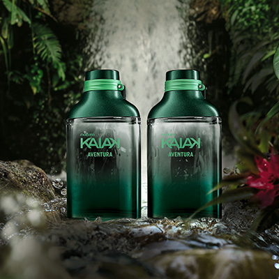 Dois Desodorantes Colônias Kaiak Aventura Masculinos com frascos de vidro transparente com detalhes em verde. Os produtos estão em frente a uma cachoeira.