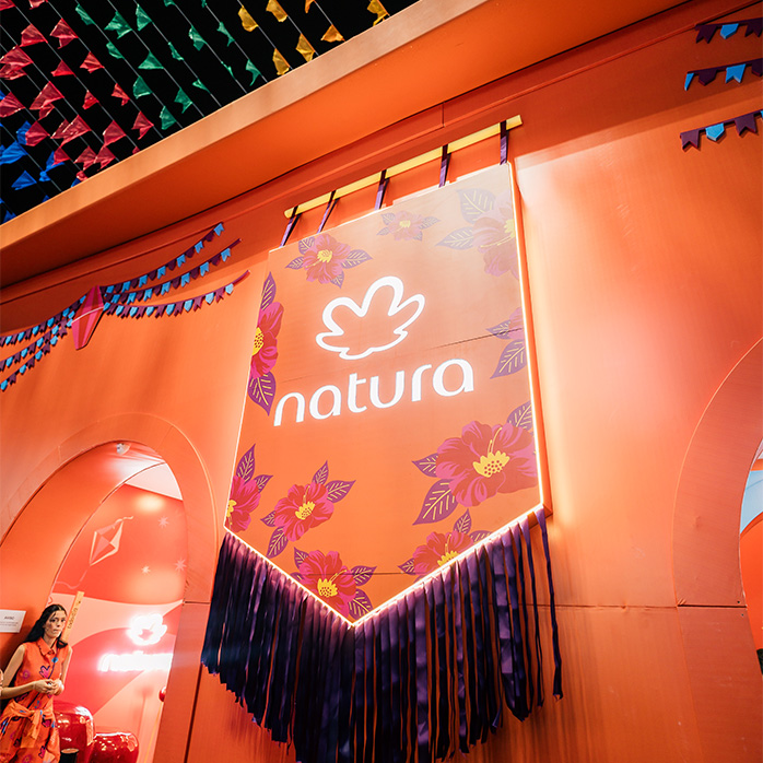 Foto de estande Natura em evento de São João, com bandeirinhas juninas no topo.