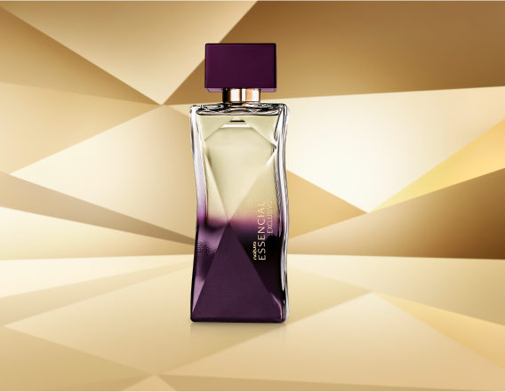 Frasco de Essencial Exclusivo Feminino, com topo transparente e base roxa, aparece em destaque no centro da tela sobre fundo multifacetado dourado, fazendo alusão ao design do frasco de Essencial.