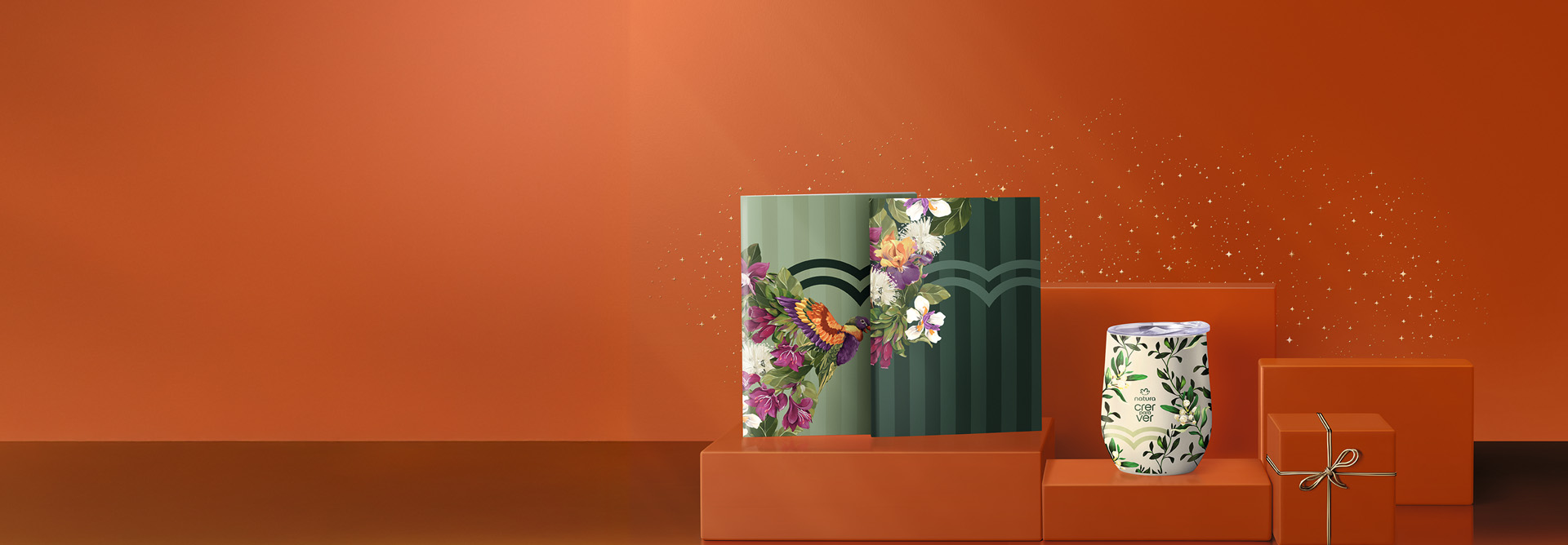Presente Natura Crer Para Ver Duo Cadernos, em tons de verde com estampa de flores, e Presente Crer Para Ver Copo Térmico, branco com estampa de folhagens e tampa transparente, sobre fundo laranja.