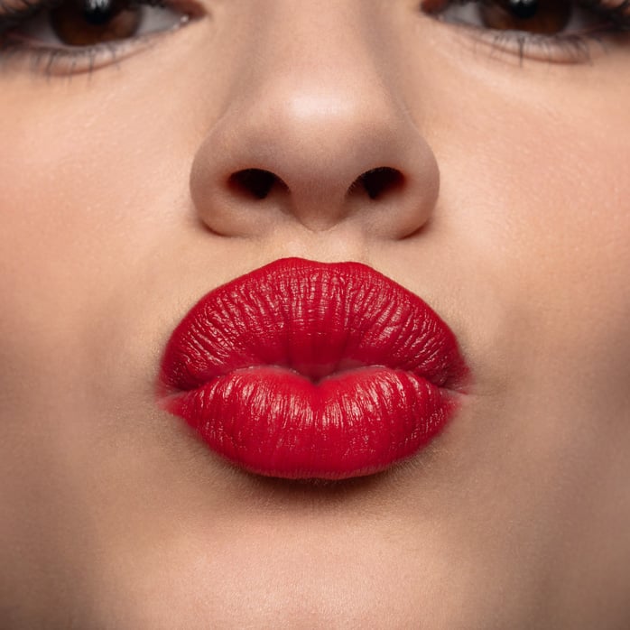 Modelo está passando gloss nos lábios. O efeito do gloss deixa os lábios brilhosos e levemente rosados.