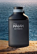 Frasco preto fosco da fragrância masculina Kaiak Extremo sobre rocha à beira do mar, com água azul e céu alaranjado ao fundo.