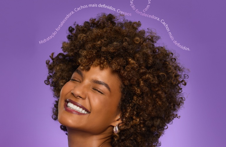 Mulher com cabelo cacheado curto sorrindo para a câmera de olhos fechados