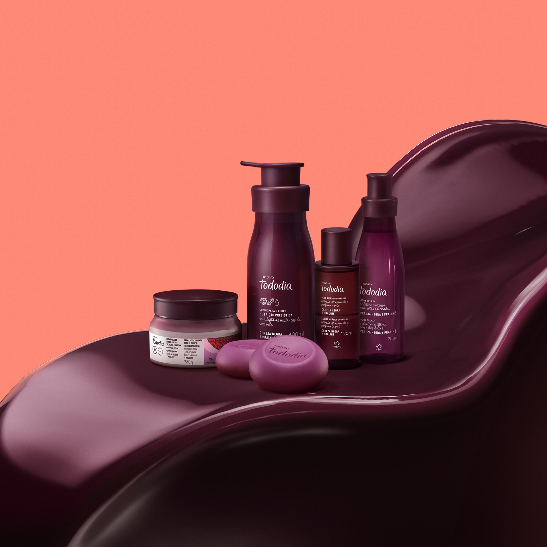 5 produtos da linha Tododia Cereja Negra e Praliné, incluindo sabonetes, cremes, óleo e body splash, repousam sobre uma textura cremosa na cor roxo intenso. Embalagens roxas com detalhes em branco.