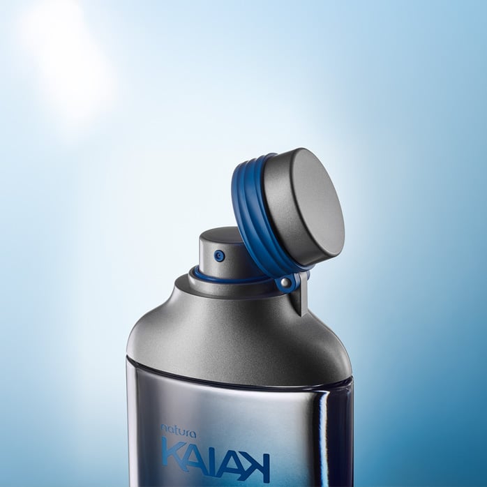 Frasco da fragrância Kaiak com tampa metálica aberta, anel azul e borrifador. Fundo degradê azul claro.