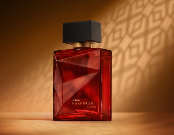 Deo Parfum Essencial Safran Masculino em frasco facetado vermelho com tampa preta. Está em fundo cor areia com sombra geométrica projetada.