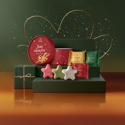 Presente Natura Tododia Sabonetes Miniaturas Estrelas em fundo verde. Estojo redondo vermelho, sachês dourado, verde e vermelho e três sabonetes estrela rosa, verde e branco sobre caixas verdes.