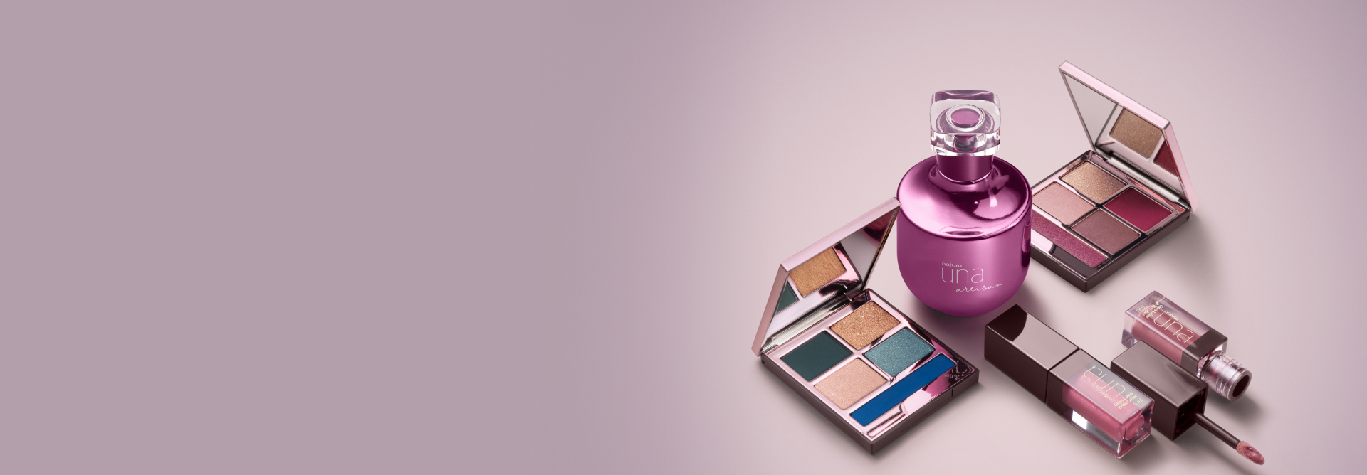 Sobre fundo lilás, frasco rosa de Deo Parfum Una Artisan, com paleta de sombras em tons frios à esquerda e em tons quentes à direita. Abaixo, embalagens fechada e aberta de gloss labial rosado.