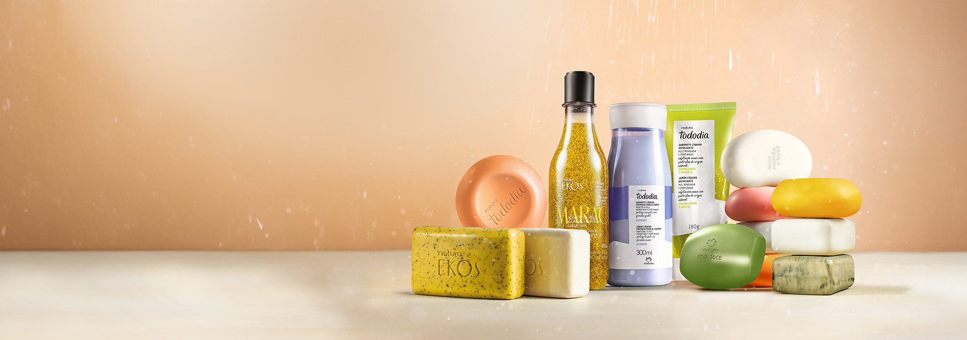 Fundo claro com tons de laranja, gotas de água caindo e diferentes tipos de sabonetes Natura.