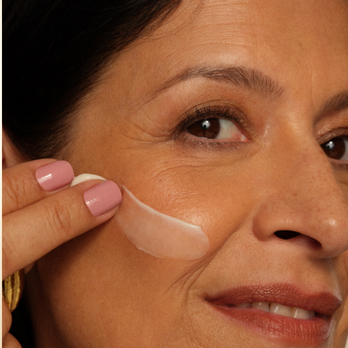 Close de foto de mulher branca de cabelos castanhos com creme na bochecha.