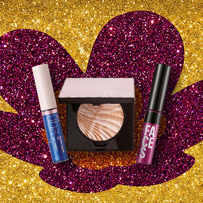 Três itens de maquiagem Natura, sendo 1 Sombra Líquida Fix Una Azul Metálico, 1 Iluminador Marmorizado Rosto e Corpo Una e Batom Líquido Faces. Fundo de glitter dourado com a flor símbolo da Natura em roxo.