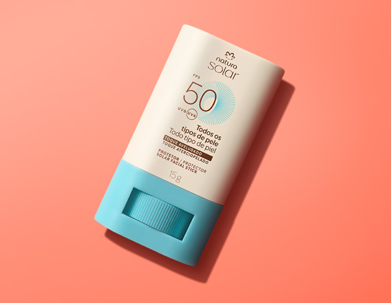 Embalagem stick com base azul e tampa creme de Natura Solar Facial FPS 50 para todos os tipos de pele, em fundo laranja