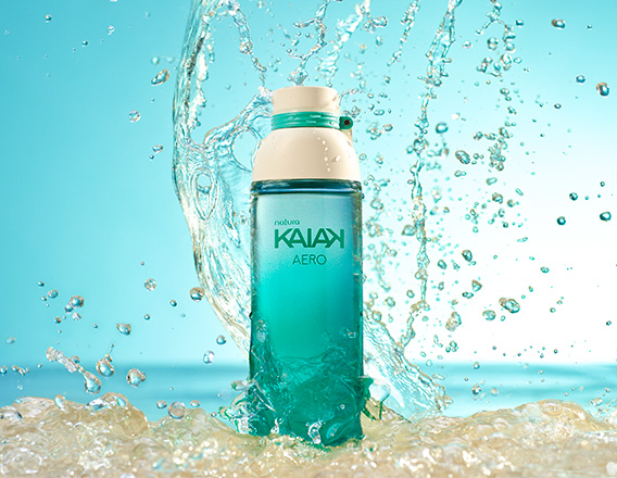 Frasco da fragrância Kaiak Aero em verde-água. Fundo azul com respingos e jatos de água em movimento.