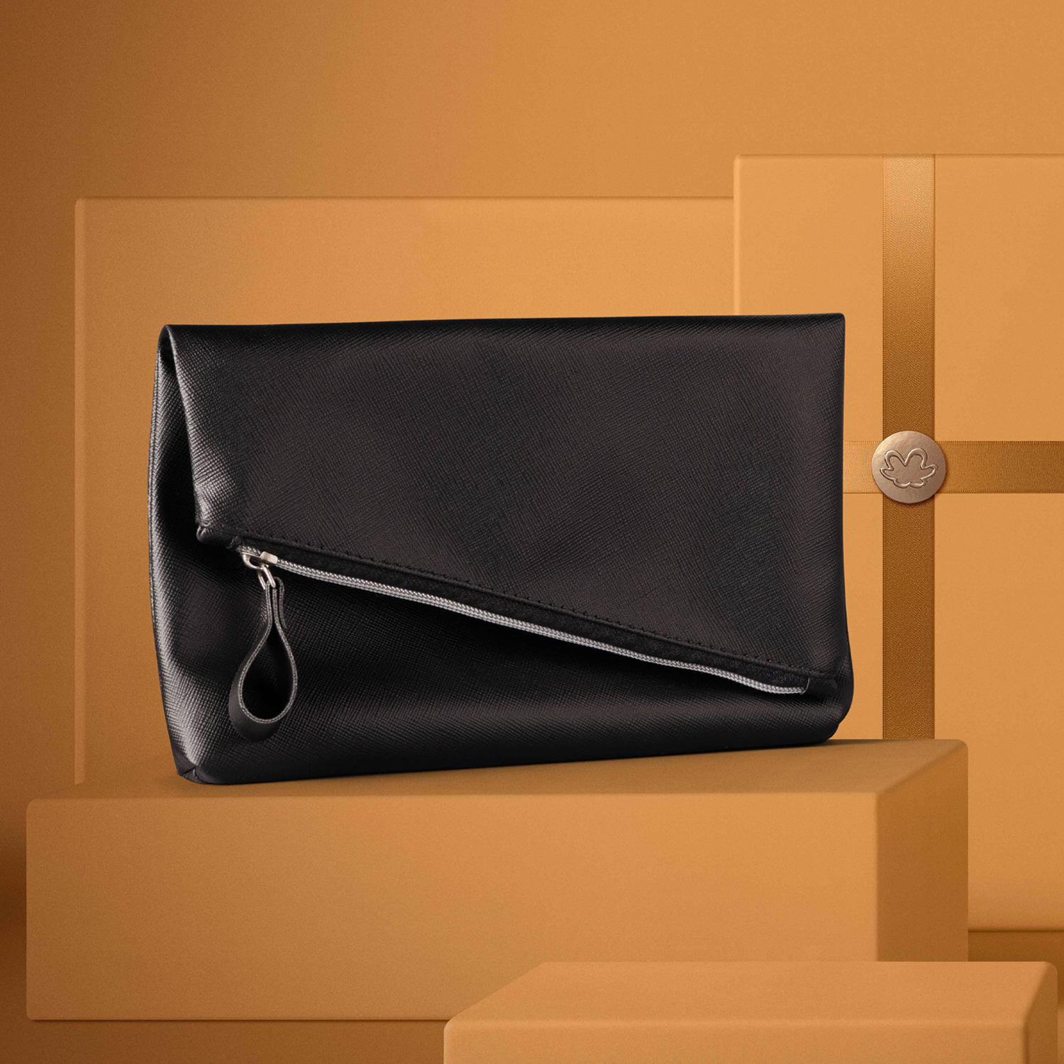 Bolsa de Mão estilo envelope feita em couro sintético preto com zíper prata repousa sobre caixas de presente. Caixas e fundo dourados. 