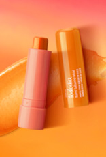 Embalagem laranja aberta de Balm Labial Tododia Manga Rosa e Água de Coco sobre textura cremosa laranja em fundo em tons de laranja e rosa.
