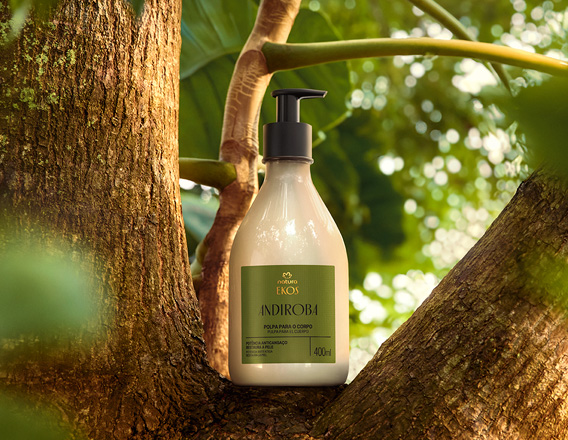 Frasco creme com válvula preta de Polpa Desodorante Hidratante para o Corpo Ekos Andiroba sobre tronco de árvore, em cenário de floresta desfocada.