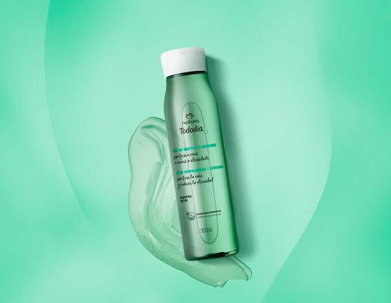 Frasco verde translúcido com tampa branca do Shampoo Detox Tododia Chá de Hortelã e Gengibre. Está sobre um rastro de gel verde em fundo degradê verde.